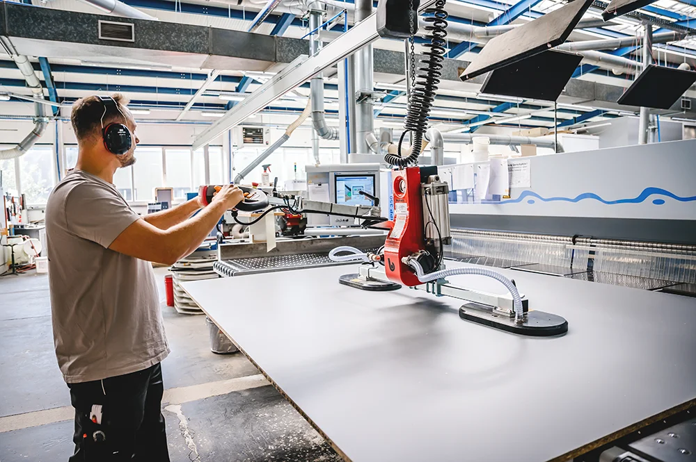 Schreiner Felix Reinehr bedient eine Maschine in seiner Werkstatt um eine Holzplatte für eine Maßanfertigung zu heben.